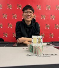 Ein Bild von einer Pokerrunde in einem Casino mit fünf Personen um einen Tisch herum sitzend, Karten haltend und Pokerchips stapelnd. Die Spieler sind konzentriert und gespannt.