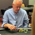 Ein Mann und eine Frau sitzen an einem Pokertisch und spielen Texas Hold'em. Der Mann hat eine Hand mit Ass und König, während die Frau eine Hand mit zwei Damen hält. Sie haben ernste Gesichtsausdr