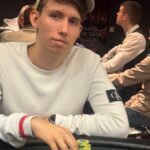 Ein Mann spielt Poker an einem eleganten Spieltisch, umgeben von anderen Spielern und einer glamourösen Atmosphäre in einem luxuriösen Casino.