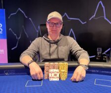 Ein Mann spielt konzentriert Poker an einem Tisch mit anderen Spielern.