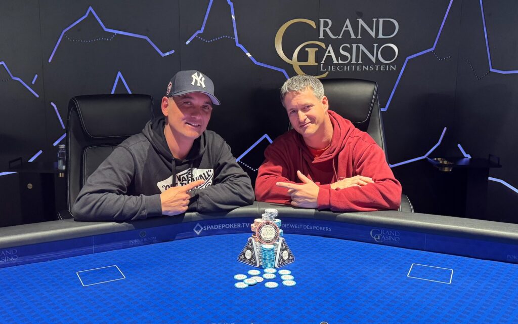 Ein Mann und eine Frau sitzen an einem Pokertisch und betrachten konzentriert ihre Karten. Die Frau hat lange braune Haare und trägt eine rote Bluse, der Mann hat kurze schwarze Haare und