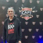 Ein Mann sitzt an einem Pokertisch, hält Spielkarten in der Hand und schaut konzentriert auf den Tisch. Um ihn herum sind Pokerchips und Getränke zu sehen.
