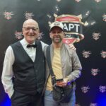 Ein Mann und eine Frau sitzen an einem Pokertisch und spielen Karten. Die Frau hat gerade gewonnen und jubelt, während der Mann enttäuscht aussieht.