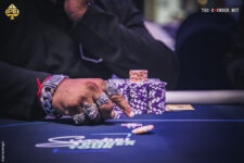 Ein professioneller Pokertisch mit grüner Filzoberfläche und einem Stapel von Pokerchips in verschiedenen Farben. Vier Spieler sitzen um den Tisch herum, jeder mit Karten in der Hand, bereit