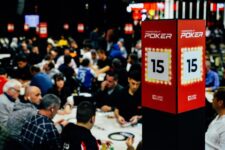 Ein Poker-Tisch mit Spielkarten, Jetons und Getränken, umgeben von mehreren Personen, die Karten halten und konzentriert spielen.