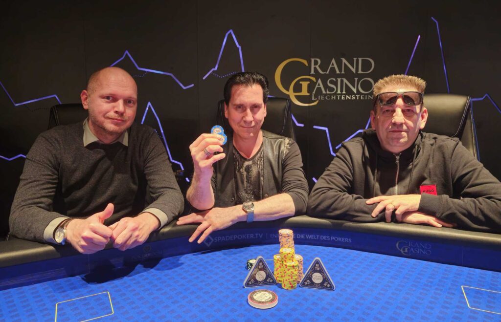 Ein Pokertisch mit grüner Filzoberfläche, umgeben von Spielkarten, Pokerchips und Getränken. Mehrere Personen sitzen um den Tisch und spielen Poker.