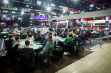 Ein Bild von einem Pokerturnier mit einer Gruppe von Menschen, die um einen Tisch herum sitzen und Karten spielen. Es gibt Chips und Getränke auf dem Tisch, während die Spieler konzentriert und ges