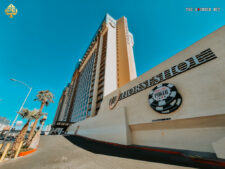 Ein belebtes Casino in Las Vegas mit vielen Menschen, die an Spieltischen sitzen und spielen. Das Casino ist mit bunten Lichtern und Dekorationen geschmückt.