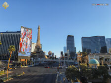 Ein belebter Abschnitt des Las Vegas Strip bei Nacht, mit den beleuchteten Fassaden des Horseshoe, Aria, Cosmopolitan und Paris Hotels im Vordergrund. Menschenmassen und Fahrzeuge bewegen