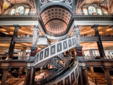 Ein lebhaftes Einkaufszentrum in Las Vegas, umgeben von hohen Gebäuden und Palmen. Menschen gehen an den Geschäften vorbei, während die Sonne scheint und der Himmel blau ist