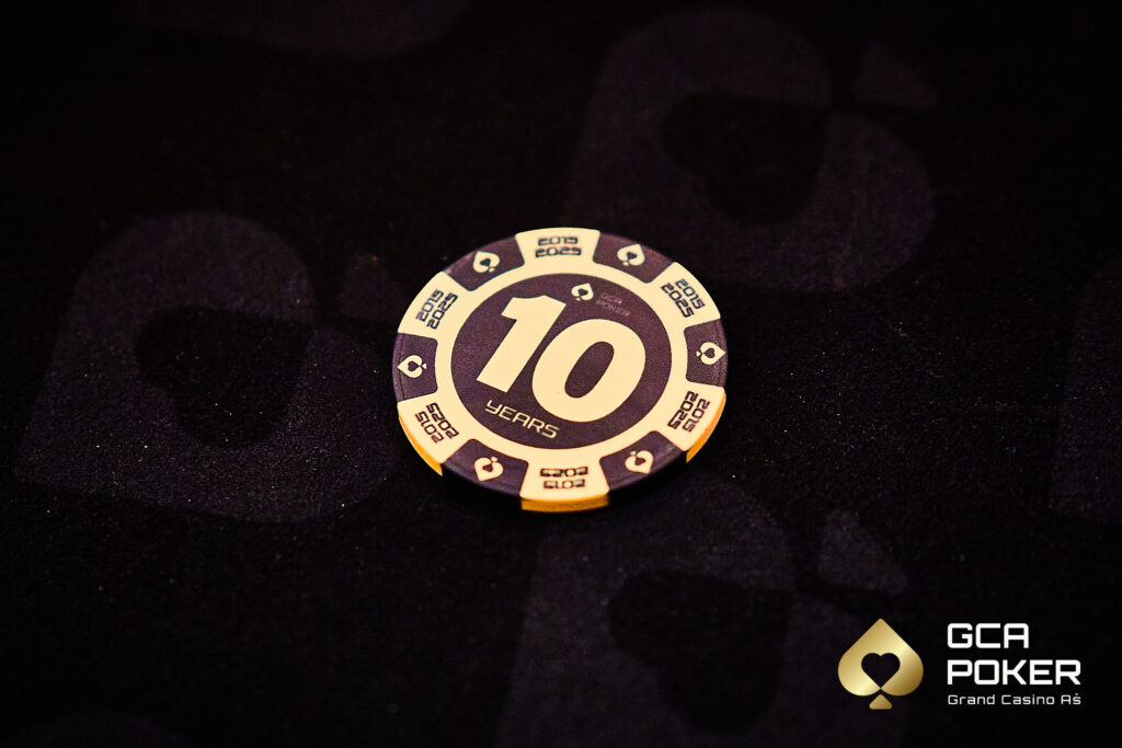 Ein Mann und eine Frau sitzen an einem Pokertisch und spielen ein intensives Pokerspiel. Der Mann hat eine Hand mit Karten in der Luft, während die Frau konzentriert auf ihre Karten schaut. Im Hinter