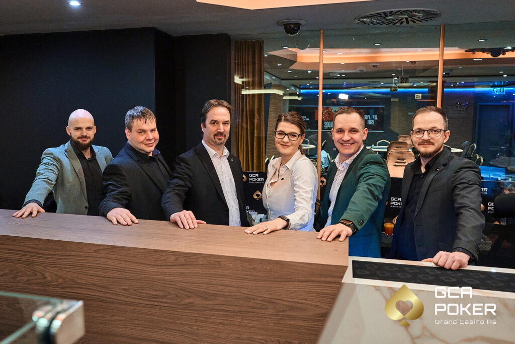 Ein professioneller Pokerspieler sitzt an einem Tisch und betrachtet konzentriert seine Karten während eines Pokerturniers. Die anderen Spieler am Tisch sind unscharf im Hintergrund zu sehen.