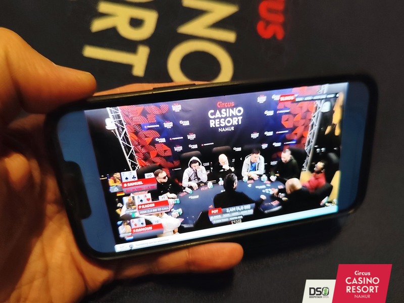 Ein Mann sitzt an einem Pokertisch und hält zwei Karten in der Hand. Er schaut konzentriert auf seine Karten, während andere Spieler im Hintergrund zu sehen sind.
