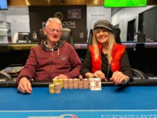 Ein Mann und eine Frau sitzen an einem Pokertisch und spielen eine Partie Poker. Der Mann hält Karten in der Hand und schaut konzentriert auf den Tisch, während die Frau ebenfalls Karten hält und lä