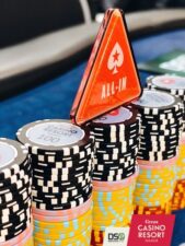 Ein Mann spielt Poker an einem Tisch in einem Casino, umgeben von anderen Spielern. Er hat eine ernste Miene und hält Spielkarten in der Hand. Die Atmosphäre ist konzentriert und gespannt