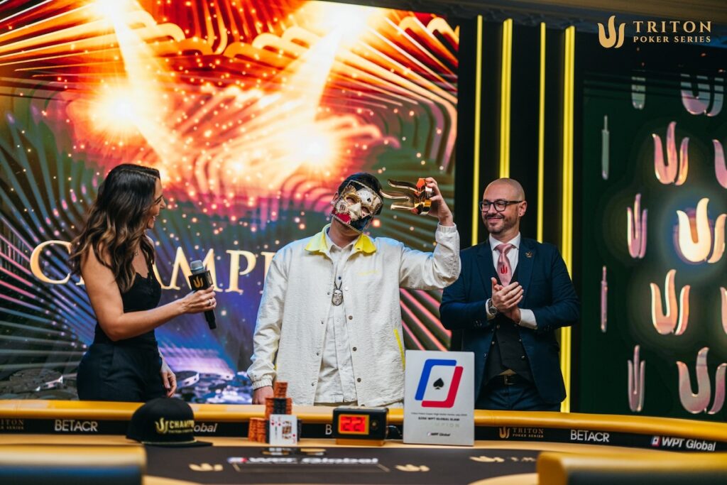 Ein Mann in einem dunklen Anzug und einer blauen Krawatte, Anatoly Filatov, feiert seinen Sieg bei Event 6 in Triton Jeju. Er steht auf einer Bühne, umgeben von jubel