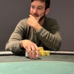 Ein Bild von einer Gruppe von Menschen, die an einem Pokertisch sitzen und Karten spielen. Es scheint eine ernsthafte und konzentrierte Atmosphäre zu herrschen.