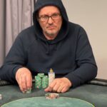 Ein professioneller Pokerspieler sitzt an einem Spieltisch in einem Casino und hält Karten in der Hand, während er konzentriert auf seine Gegner schaut.