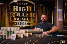 Ein Mann sitzt an einem Pokertisch mit einem Stapel Chips vor sich. Er schaut konzentriert auf seine Karten, während andere Spieler im Hintergrund zu sehen sind.