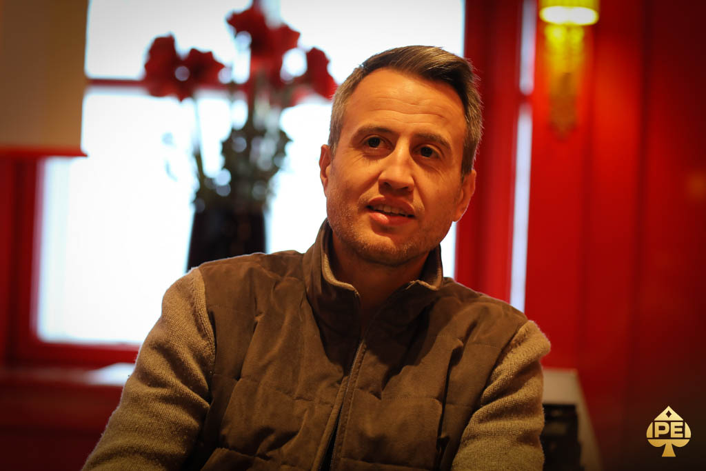 Ein Mann sitzt an einem Pokertisch und wirft einen intensiven Blick auf seine Karten. Er sieht konzentriert und fokussiert aus.