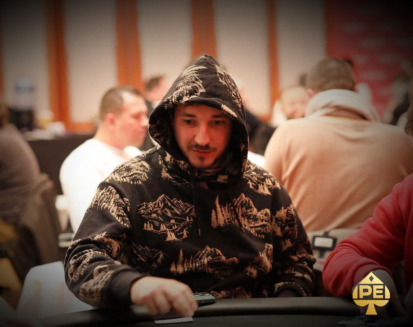 Ein Mann in einem schwarzen Anzug sitzt an einem Pokertisch und hält Karten in der Hand. Er schaut konzentriert auf seine Karten und wirkt entschlossen.