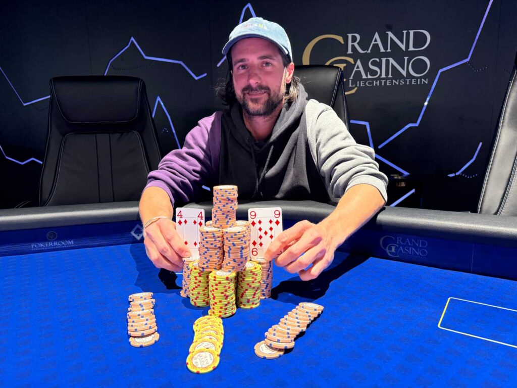 Ein Mann und eine Frau spielen Poker in einem eleganten Casino. Der Mann hat einen Anzug an und die Frau trägt ein rotes Abendkleid. Sie sitzen an einem grünen Pokertisch, auf dem Karten und