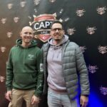 Ein Mann spielt Poker an einem Tisch in einem eleganten Casino. Er hat eine Hand mit Spielkarten und Chips vor sich liegen, während er konzentriert auf seine Karten schaut. Im Hintergrund sind andere Spieler