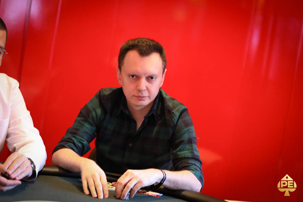 Ein Mann sitzt an einem Pokertisch und hält Karten in der Hand, während er konzentriert auf das Spiel schaut.