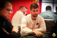 Ein Mann sitzt an einem Pokertisch, konzentriert und mit einem ernsten Gesichtsausdruck. Er hat kurze dunkle Haare und trägt ein schwarzes Hemd.