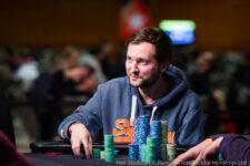 Ein Mann sitzt an einem Pokertisch bei einem Turnier in Prag im Jahr 2017. Er hat eine ernste Miene und betrachtet seine Karten konzentriert. Im Hintergrund sind andere Spieler und ein