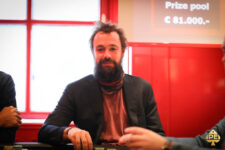 Ein Mann in einem schwarzen Anzug und weißem Hemd sitzt an einem Pokertisch und hält Pokerchips in der Hand.