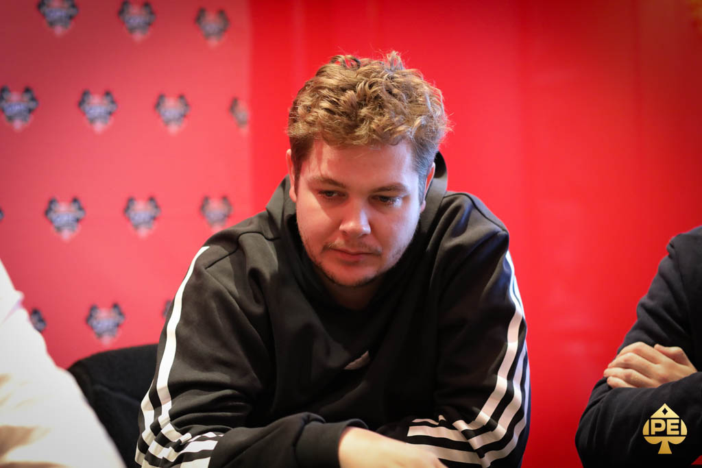 Ein Mann namens Oliver Weis sitzt lächelnd an einem Pokertisch und hält Karten in der Hand. Sein Blick ist konzentriert und selbstbewusst.