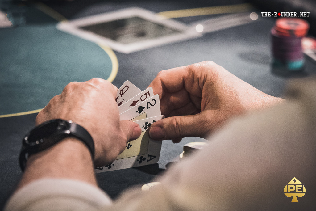 Ein Poker-Tisch mit grünen Filz, Spielkarten und Pokerchips, auf dem eine Partie Pot Limit Omaha (PLO) stattfindet. Vier Spieler sind zu sehen, die ihre Karten prüfen und