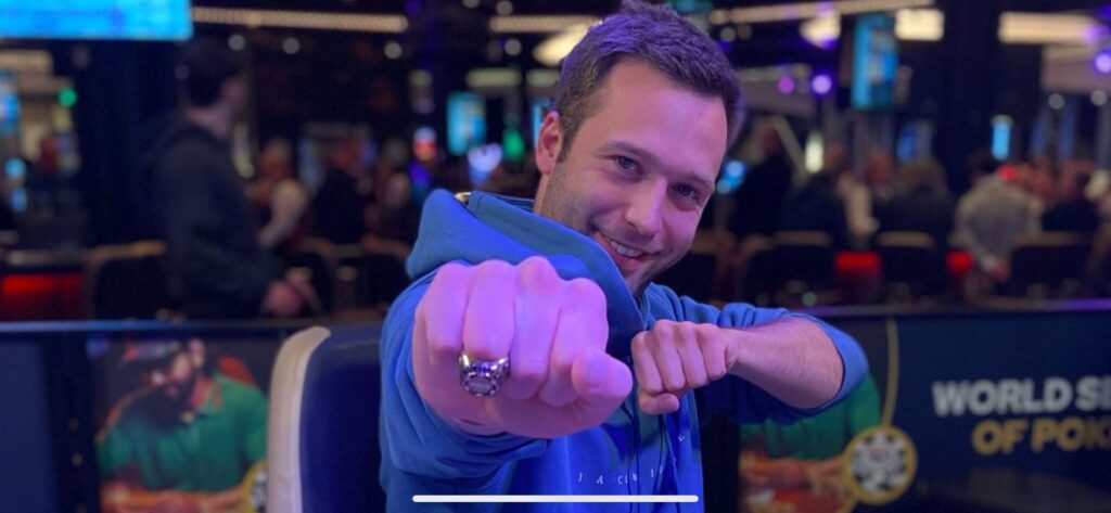 Ein Spieler mit Sonnenbrille und Kappe hebt seinen Chipstack während eines Pokerturniers in einem Casino.