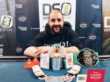 Ein Mann sitzt an einem Pokertisch und hält zwei Karten in der Hand. Er schaut konzentriert auf den Tisch, wo Chips und Karten liegen. Im Hintergrund sind weitere Spieler zu sehen.