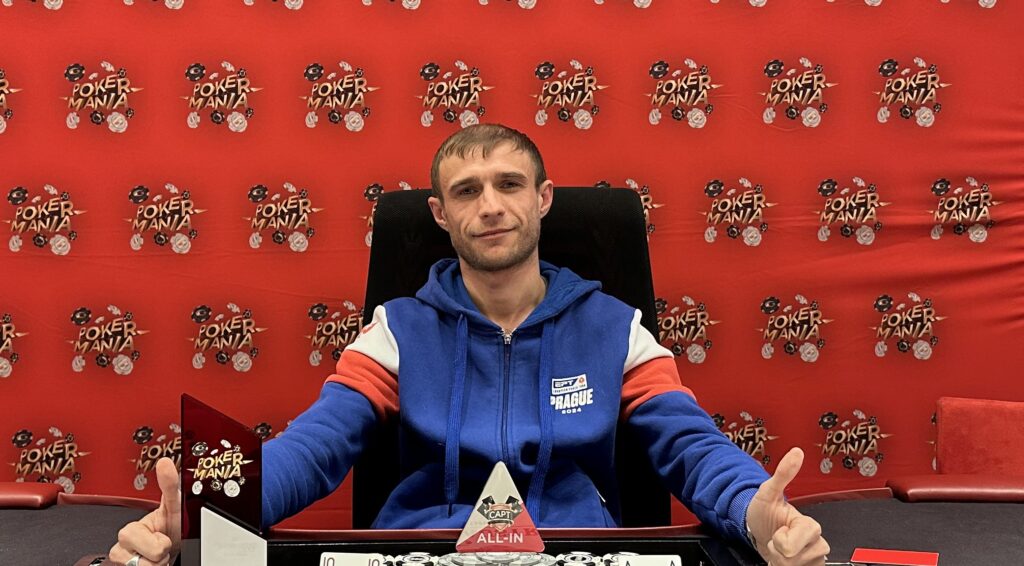 Ein Gruppenfoto von Pokerspielern, die an einem Tisch sitzen und Karten halten. Ein Spieler hat gerade gewonnen und jubelt, während die anderen Spieler unterschiedliche Reaktionen zeigen. Im Hintergrund sind Pokerch