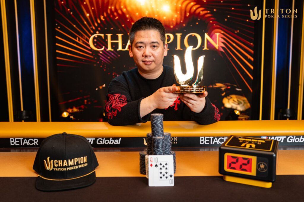 Ein Mann in einem dunklen Anzug und einer Sonnenbrille, der jubelnd die Hände in die Luft wirft, umgeben von einer Menschenmenge in einem Casino. Im Hintergrund sind Pokertische und Spieler zu
