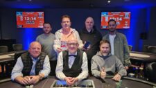 Ein Gruppenbild von vier Freunden, die fröhlich lachen und zusammen an einem Pokertisch sitzen. Sie haben Karten in der Hand und Chips vor sich liegen. Das Ambiente ist entspannt und gemütlich