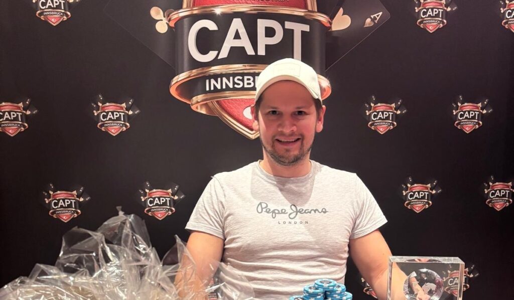 Ein Mann in einem eleganten Anzug hält stolz einen Pokal in die Luft, umgeben von jubelnden Menschen.