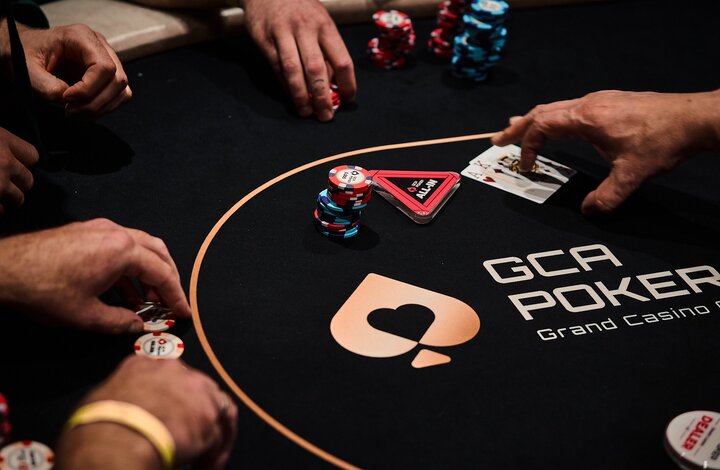 Ein Poker-Turnier mit einer Gruppe von Spielern, die um einen Tisch herum sitzen und Karten spielen. Der Dealer mischt gerade die Karten.