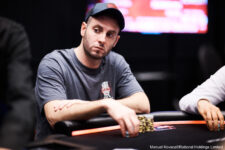 Ein Mann sitzt an einem Pokertisch in einem Casino, umgeben von anderen Spielern. Er hält Karten in der Hand und schaut konzentriert auf den Tisch.