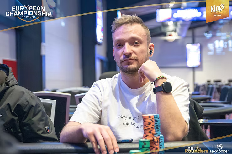Ein Mann sitzt an einem Pokertisch, umgeben von Chips und Karten. Er hat eine konzentrierte Miene und trägt ein schwarzes Hemd.