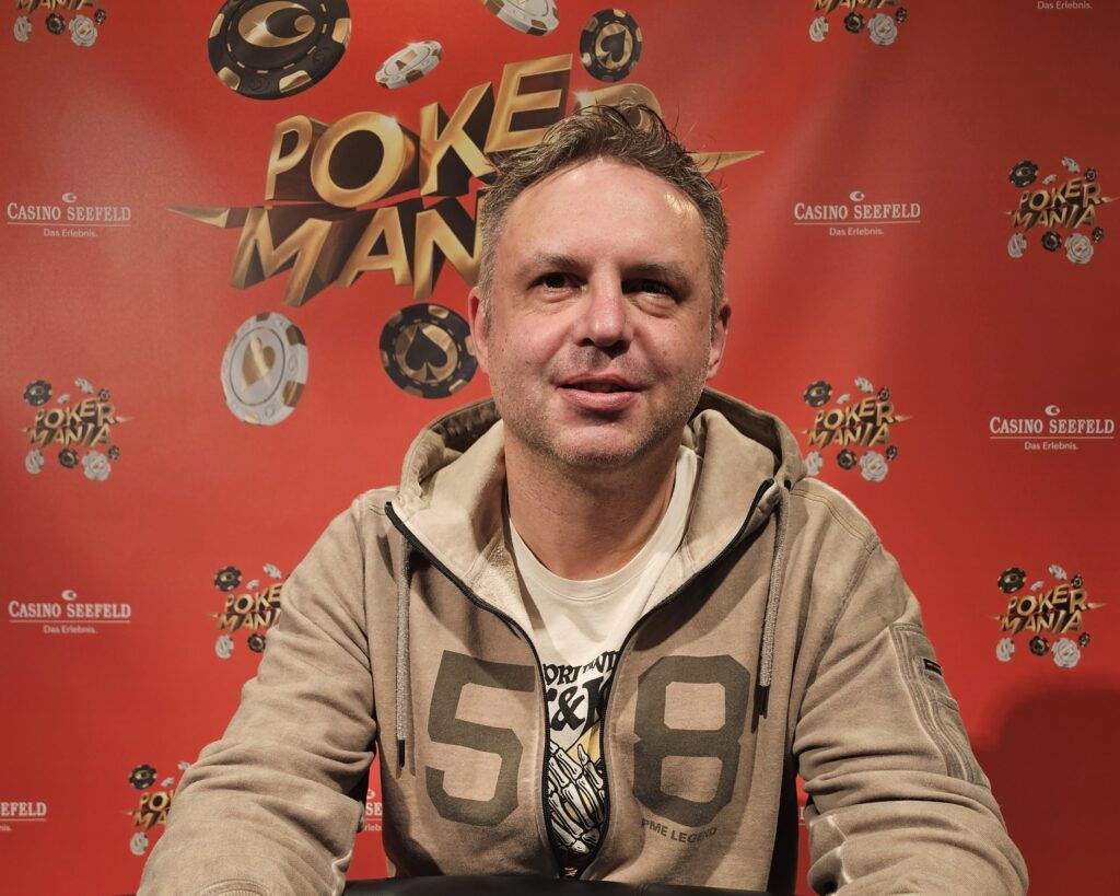 Ein Mann in einem schwarzen Anzug spielt Poker in einem eleganten Casino in Seefeld, Österreich. Er hält Karten in der Hand und konzentriert sich auf das Spiel. Im Hintergrund sind andere Spieler und