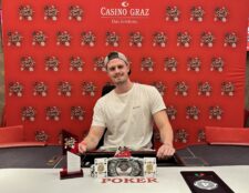 Ein Mann freut sich über seinen Sieg beim Pokerspiel. Er hält stolz seine Karten in der Hand und lächelt glücklich. Um ihn herum stehen andere Spieler, die enttäuscht wirken