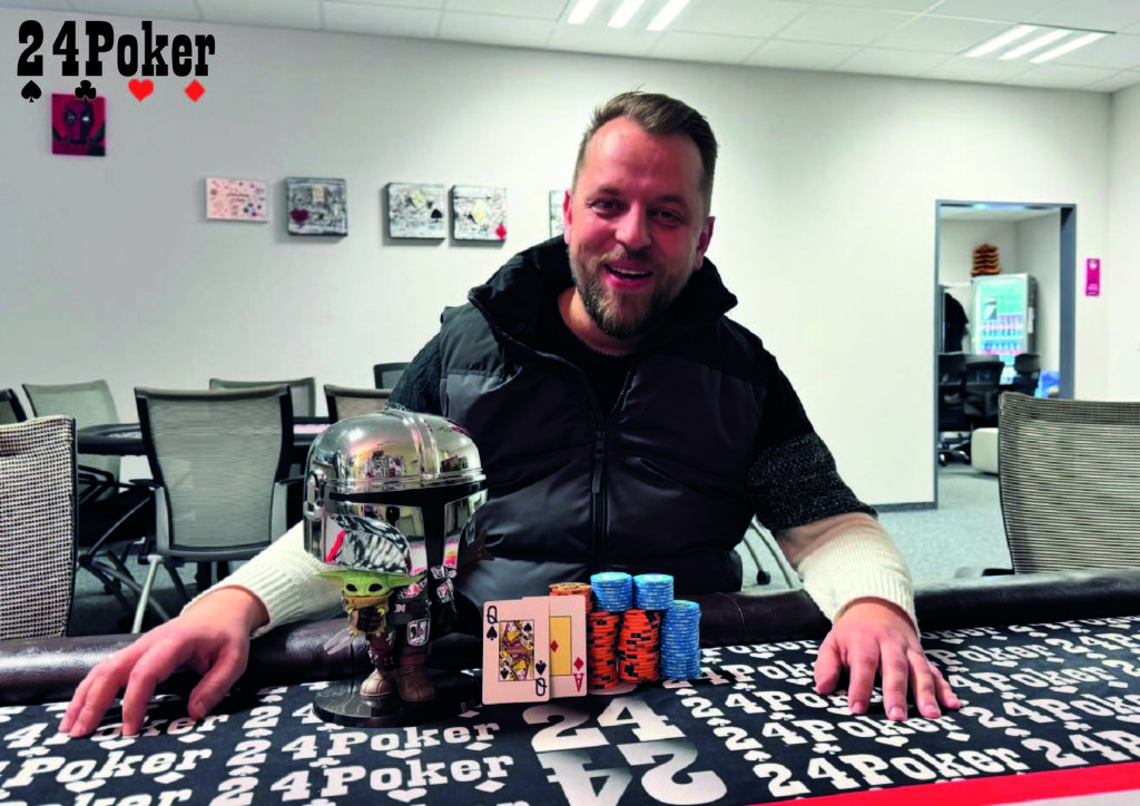 Ein Gruppenfoto von Pokerspielern, die lächelnd und jubelnd ihre Hände in die Luft strecken. In der Mitte steht ein Spieler mit einem großen Pokal in der Hand.