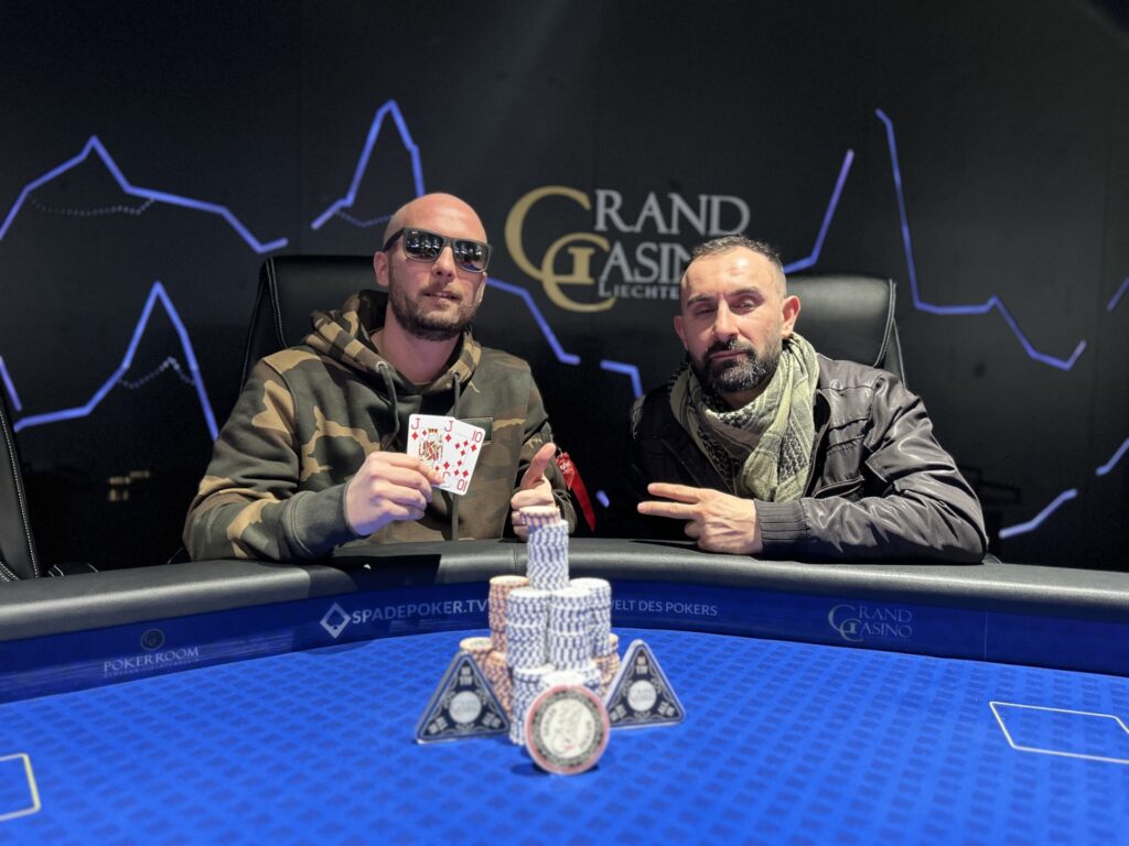 Ein Mann in einem Anzug steht jubelnd mit erhobenen Händen vor einem Pokertisch, auf dem Pokerchips und Spielkarten liegen.