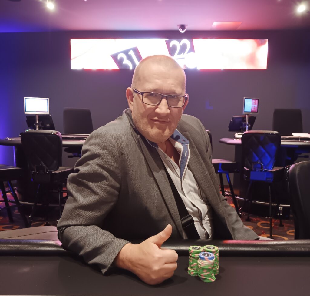 Ein Mann und eine Frau spielen Poker in einem eleganten Casino. Der Mann hält Karten in der Hand, während die Frau mit ernstem Gesichtsausdruck ihre Chips betrachtet. Die Szene strahlt Spannung und