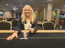 Ein Mann und eine Frau spielen Poker an einem Tisch mit grünem Filz. Der Mann hält Karten in der Hand und schaut konzentriert auf seine Gegnerin, die ebenfalls Karten hält und lächelt
