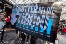 Ein Mann und eine Frau sitzen an einem Pokertisch, sie halten Karten in den Händen und schauen konzentriert auf den Tisch. Im Hintergrund sind Pokerchips und Getränke zu sehen.
