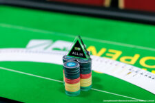 Ein Bild eines Pokertisches mit grünen Filz, Stapel von Pokerchips, Karten und Händen von Spielern.